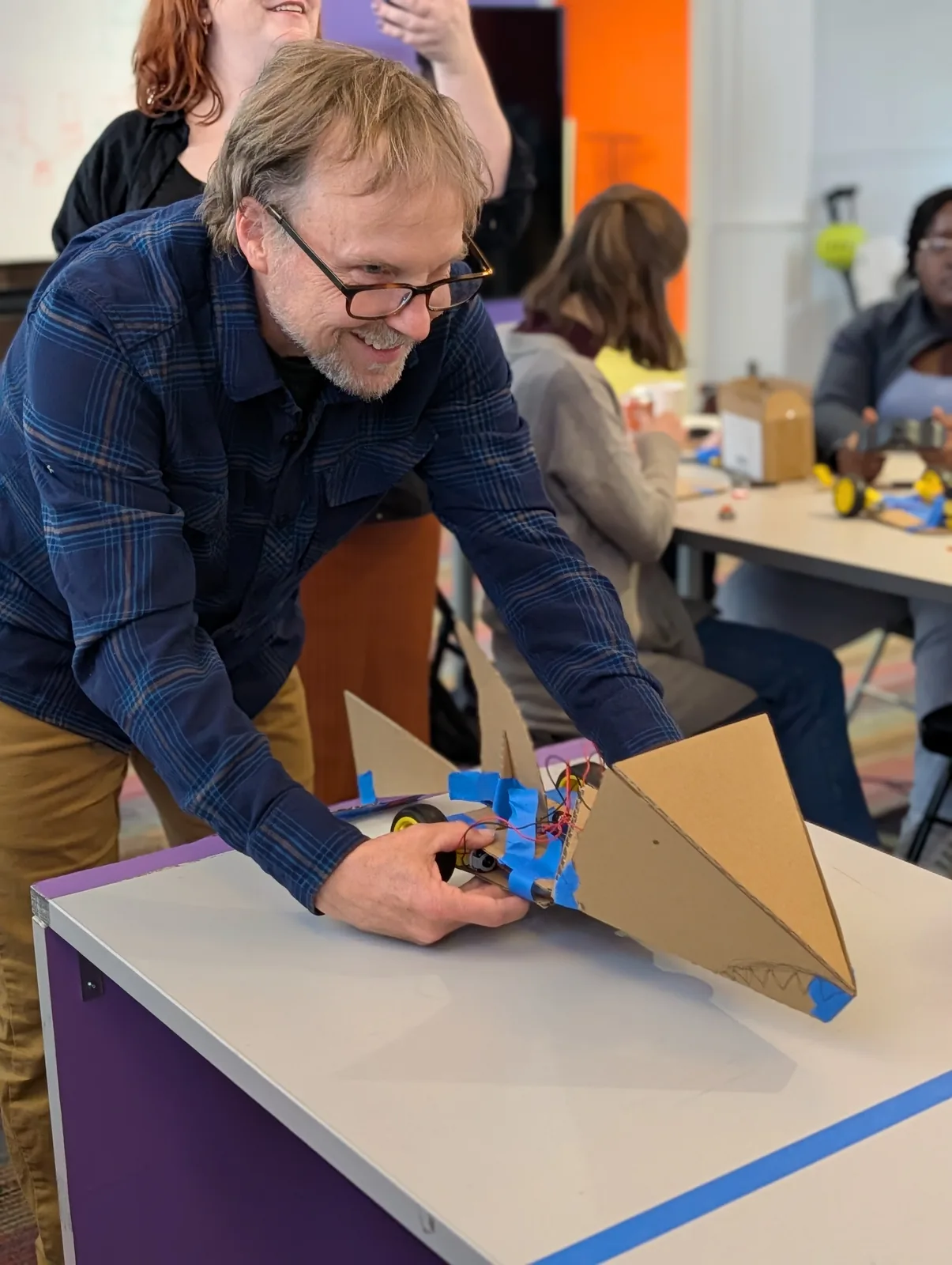 An adult workshop participant smiling as he tests a cardboard robot