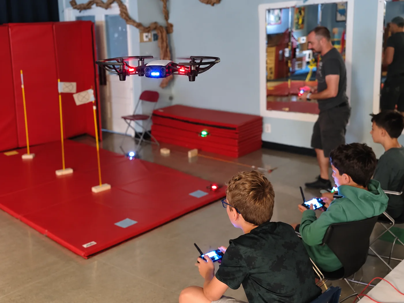 Children piloting drones through an indoor obstacle course with an instructor