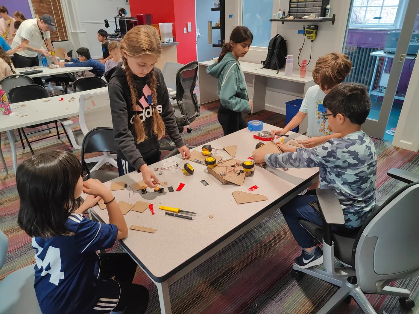 Students building cardboard robots together around a workshop table