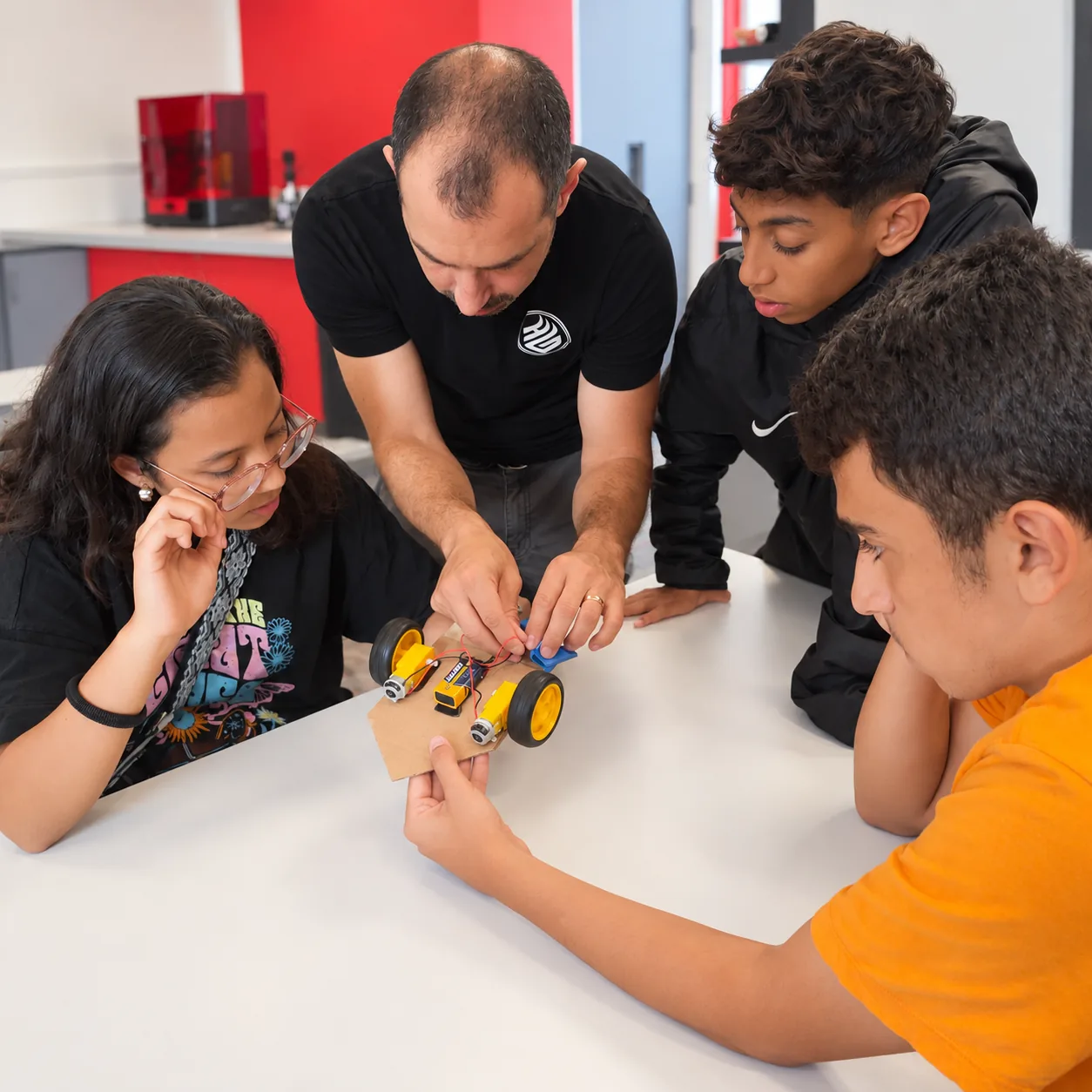 An instructor helping three young makers connect a robot's electronics