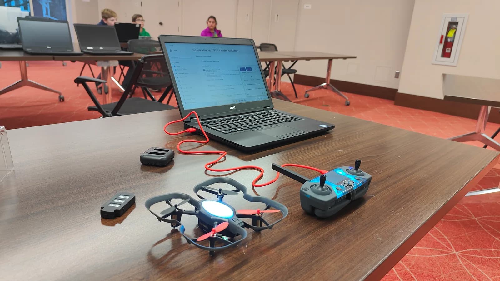 A small drone and controller beside a laptop