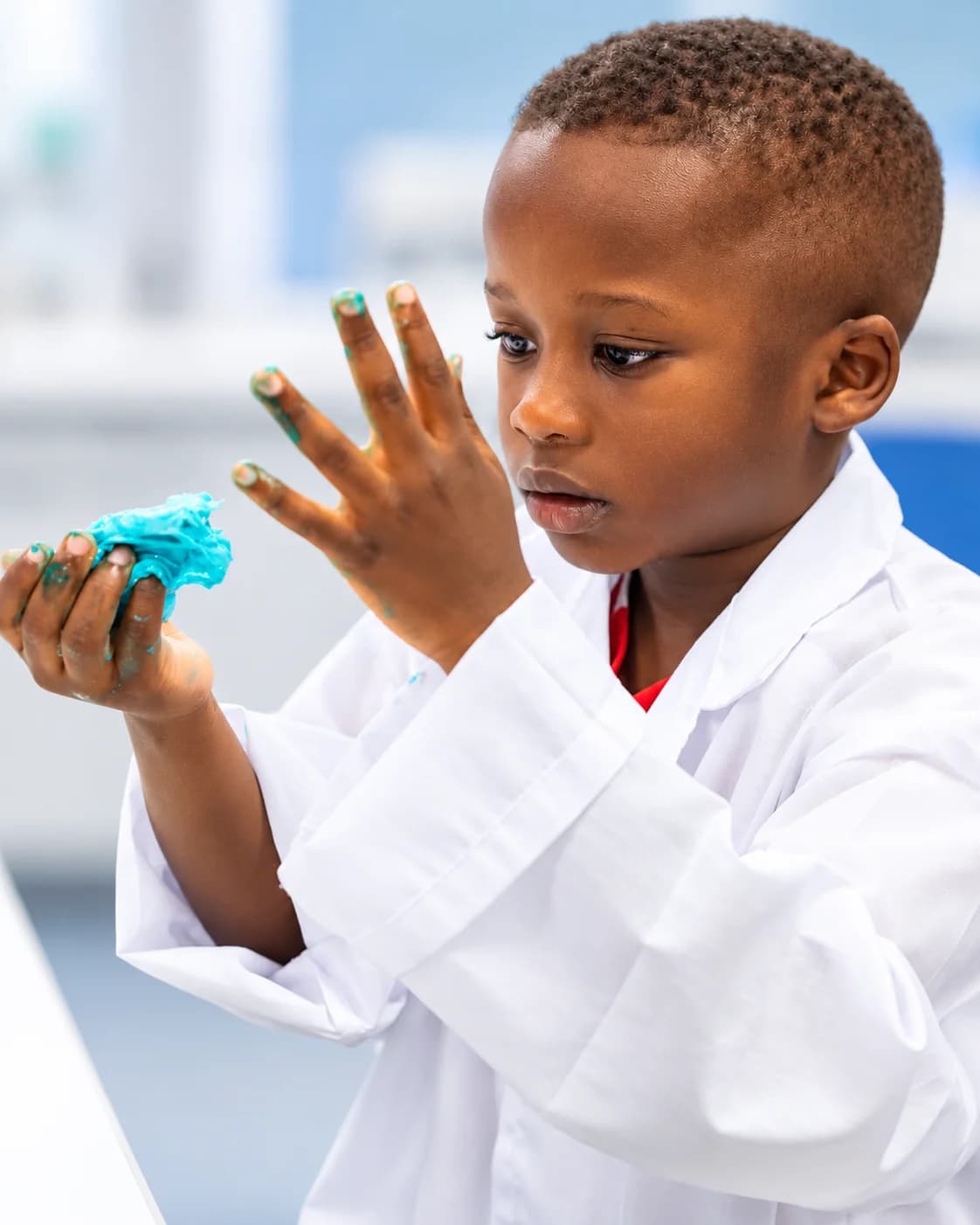 A child in a lab coat examining blue slime on their hands
